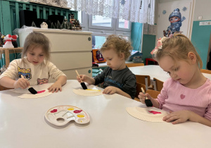 Dzieci przy stole malują farbami kolorowymi talerzyki