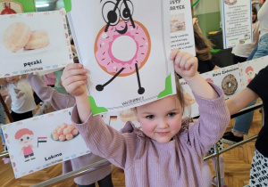 Dziewczynka pokazuje pączka w uniesionymi ekoma i jedną nogą w górze