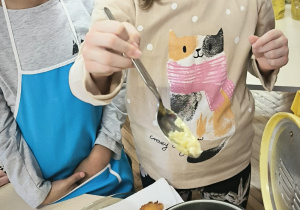 Dziewczynka łyżką wklada kulkę pączka do frytownicy