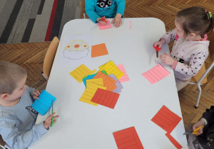 Dzieci siedza przy stoliku z nożyczkami