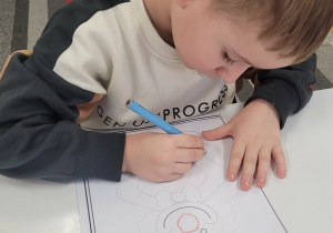 Chłopiec łączy kropki niebieską kredką