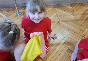 Dziewczynka podnosi woreczek zżółty palcami stóp