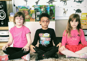 Dzieci siedza przed makietą z dinozaurami