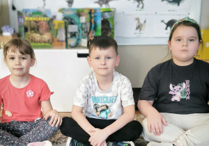 Dzieci siedzą przed makietą z róznymi dinozaurami