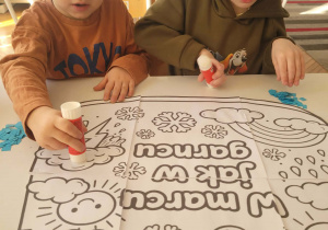 Chłopcy siedzą przy stoliku z namalowanym garnkiem marcowym