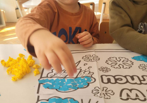 Chłopiec wykleja niebieskim papierem chmurkę