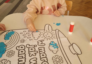 Dziewczynka wykleja niebieskim papierem chmurkę deszczową