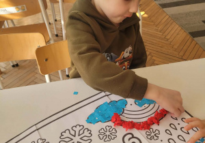 Chłopiec kulkami z bibuły wykleja tęczę