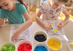 Dziewczynki wyklejają kolorową bibuła stworka emocji