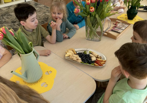 Dzieci siedzą przy stole i jedzą owoce