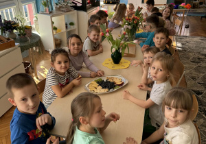 Dzieci siedzą przy stole z kwiatami i owocami