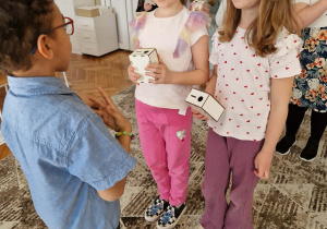 Chłopiec stoi przed dwoma dziewczynkami z prezentami