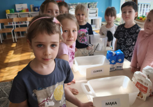 Dzieci stoją trzymając w reku napisy mąka, cukier