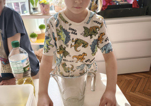 Chłopiec przyczepia do dzbanka napis woda