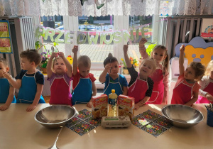 dzieci stoją w fartuszkach przed stolikami