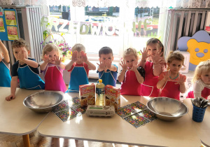 dzieci stoją w fartuszkach przed stolikami