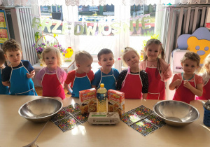 dzieci stoją w fartuszkach przed stolikami