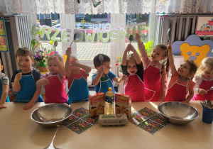 dzieci stoją w fartuszkach przed stolikami