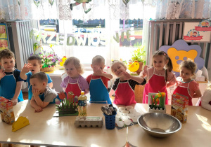 dzieci stoją w fartuszkach przed stolikami