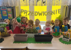 dzieci stoją przed doniczkami, ziemią i cebulkami pozując do zdjęcia