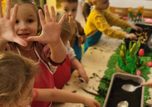 dzieci wsypują łyżkami ziemię do donicy