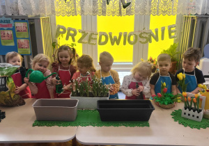 dzieci stoją przed doniczkami, ziemią i cebulkami pozując do zdjęcia