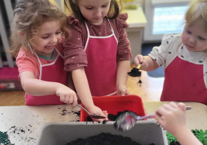 dzieci wsypują łyżkami ziemię do donicy