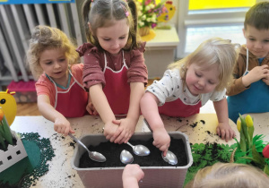 dzieci wsypują łyżkami ziemię do donicy