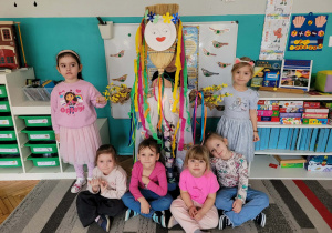 Dzieci stoją i siedzą z kukłą Marzanny