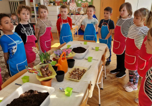 Dzieci stoją przed stołami z doniczkami