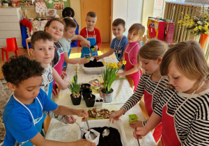 Dzieci nabierają ziemię na łyżki i wrzucają ją do doniczek