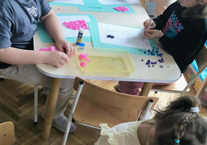 Dzieci przy stoliku wyklejają bibułą hiacynta