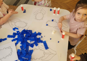 Dzieci siedzą przy stoliku z niebieską bibułą