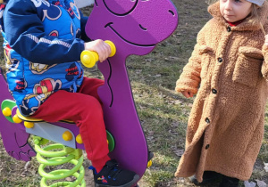 chłopiec buja się na bujawce, dziewczynka stoi obok niego