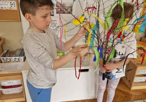 Chłopiec wiąże na gałązce wstażkę