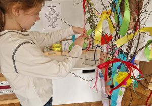 Dziewczynka zakłąda na gałązkę kolorową wstążkę