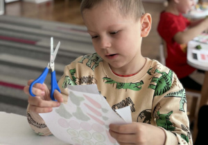 Chłopiec z nozyczkami siedzi przy stoliku