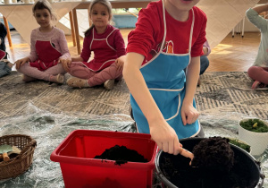 Chłopiec nabiera z wiaderka ziemę do kwiatów