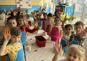 Dzieci stoją przy stole z małymi doniczkami