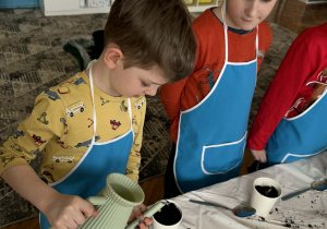 Chłopiec podlewa sowją doniczkę z rośliną