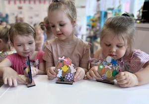 Trzy dziewczynki pokazują swoje ozdobione drewniane pisanki