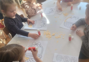 Dzieci siedzą i przyklejają kwadraty na koszyczek