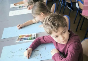 Dzieci przy stole malują w pisance królika