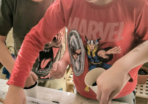 Chłopiec nabiera ziemię na szpadelek i wsypuje do doniczki