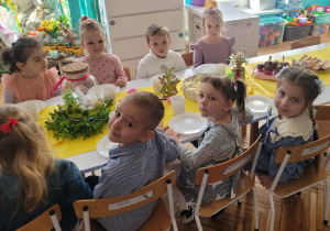 Dzieci siedza na krzesłach przy stole wielkanocnym