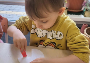 chłopiec nakleja elementy na pracę plastyczną