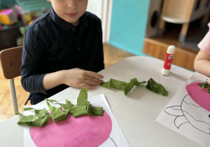 Chłopiec drze na kawałki zieloną bibułę