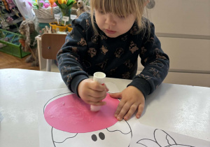 Dziewczynka smaruje klejem różowy karton