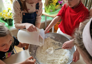 Dziewczynkki wlewają wodę i mieszają w misce ciasto