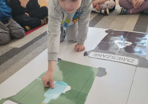 Chłopiec wkłada do kosz szklaną butelkę